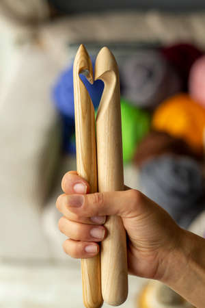 Two wooden knitting needles in a female hand on the background of multi-colored merino skeins in the shape of a heartの写真素材