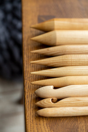 Assorted wooden knitting needles lie on a wooden table, in the background a blurred gray plaid merino woolの写真素材