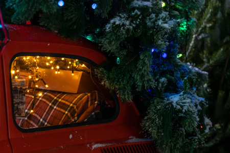 Rear side window of a red snow-covered rare car with festive New Years lights and a Christmas tree.の写真素材