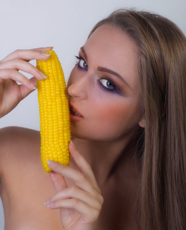 Beautiful portrait of a girl holding a juicy head of corn, looks into the frame, bright makeの写真素材