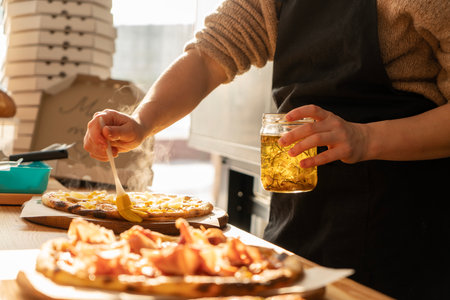 Close-up of a man and a womans hands are preparing pizza in the kitchen in a restaurant, laying out the meat and oiling. on a sunny dayの写真素材