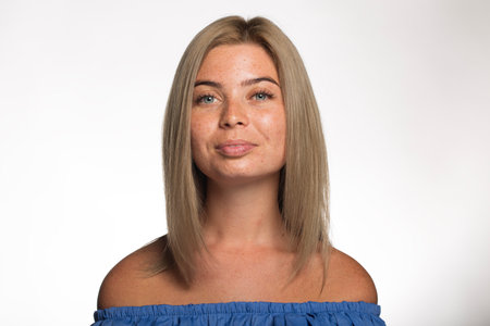 Beautiful girl with freckles with loose blond hair looks at the camera on a white backgroundの写真素材