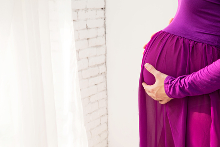 pregnant woman in purple dress put her hands on her bellyの写真素材