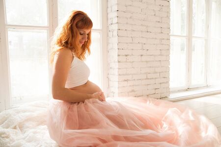 pregnant woman in a taffeta skirt sits near the windowの写真素材
