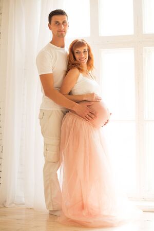 a pregnant woman in a white top and a tuxedo skirt and her husbaの写真素材