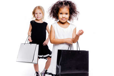 Little fashionable girls girlfriends of two different nationalities posing on a white background with shopping bags. Horizontal photoの写真素材