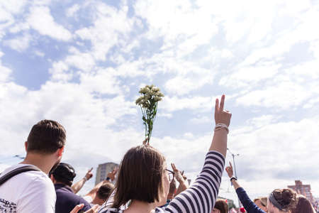 Minsk, Belarus - August 15, 2020. Protest actions in Minsk. Woman with hands raised up. In one hand she holds flowers and in the other she shows the sign of victory. Horizontal photoのeditorial素材