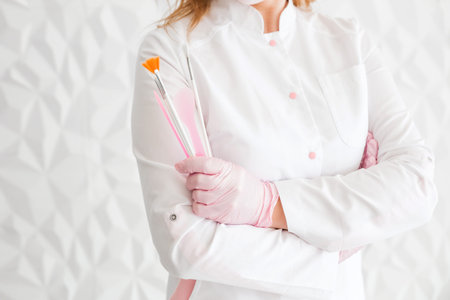 Professional beautician with brushes in hands. Woman beautician posing against white wall...