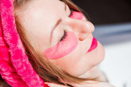 Beautiful young woman in a pink cosmetic bandage and with pink birds under her eyes poses in front of the camera in a white ceramic bath in a sunny bathroom. Girl smiles and lies with closed eyes. Horizontal photoの写真素材