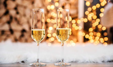 Beautiful two glasses of champagne standing in the background of a blurred room with a decorated Christmas light and fireplace. Soft focus. Horizontal photoの写真素材