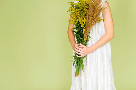 Girl in white linen dress posing on a green background with a bouquet of wildflowers. Horizontal photoの写真素材