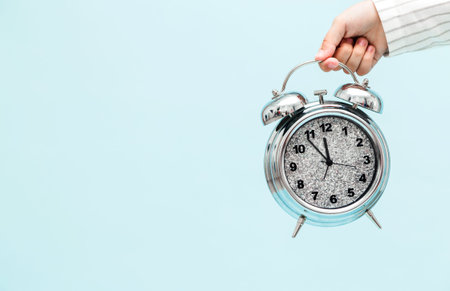 Child hand holding alarm clock isolated on blue background. Horizontal photo