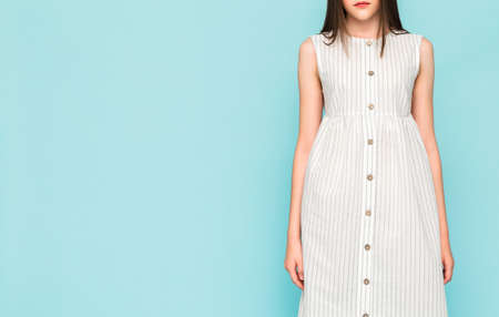 A slender girl in a white linen dress posing on a blue background. Horizontal photoの写真素材
