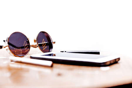 Cigarettes, sunglasses, glasses and a telephone lie on a wooden table on a white background. Brutal man set. Horizontal photoの写真素材
