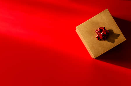 Cardboard box with red bow on red background. Horizontal photoの写真素材