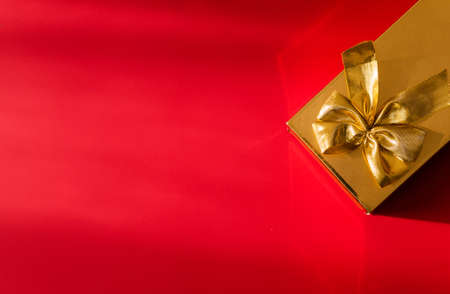 Gold color gift wrap with gold bow on red background. Horizontal photoの写真素材
