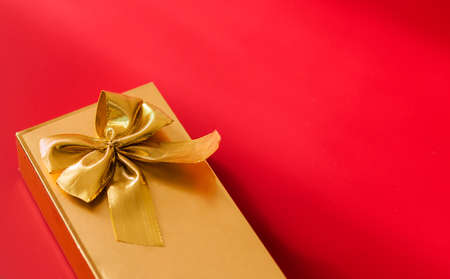 Gold color gift wrap with gold bow on red background. Horizontal photoの写真素材