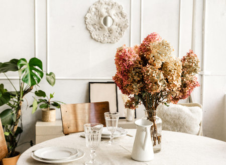 Part of the interior of the room. A vase of flowers stands on a round table against a light wall....