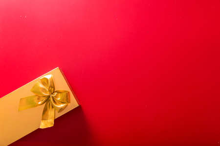 Gift in a golden package with a bow on a red background. Horizontal photoの写真素材