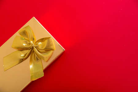 Gift in a golden package with a bow on a red background. Horizontal photoの写真素材