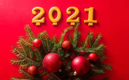 The numbers 2021 and a Christmas tree branch with red toy ballson red background, advertising photo. Horizontal photoの写真素材