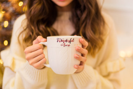 A girl in a white sweater and leggings holds a large white cup in her hands. Horizontal photo