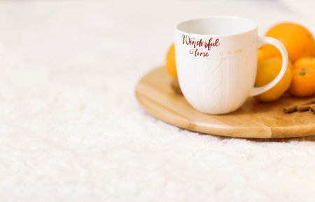 A white cup with the inscription Wonderful Winter stands on a wooden tray, pallesins and cinnamon...