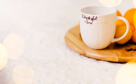 A white cup with the inscription Wonderful Winter stands on a wooden tray, pallesins and cinnamon lie next to it. The tray is on a soft white carpet. Horizontal photoの写真素材