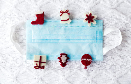 Medical mask with christmas pins on white knitted background. Horizontal photo