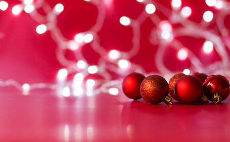 Toy Christmas balls of red color lie on a red background. Christmas garland in the background. Horizontal photoの写真素材