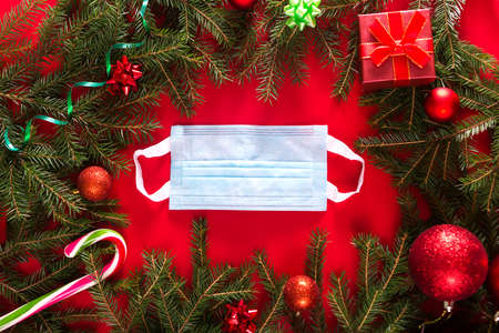Christmas decorative background with Christmas tree on a medical mask on red background top view, flat layout. Horizontal photoの写真素材