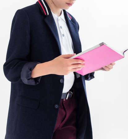 Photo of A schoolboy stands on a white background in a school uniform - trousers, a jacket and a shirt. A boy holding an open textbook in his handsの写真素材