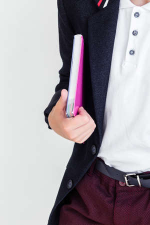 Photo A schoolboy stands on a white background in a school uniform - trousers, a jacket and a shirt. A boy holding a textbook under his armの写真素材