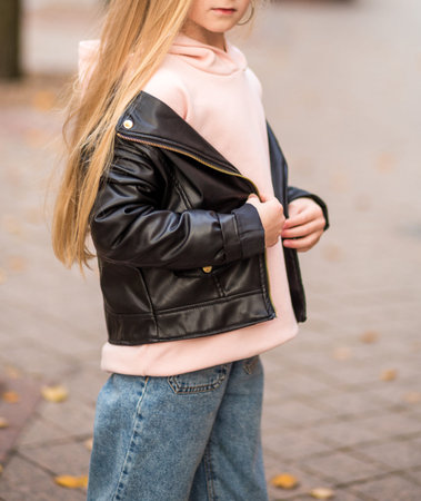 Girl in jeans, pink hoodie and black jacket posing on a city street. Photo