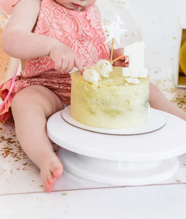 Little girl in a pink suit eats a cake with her hands on the background of a festive decorationの写真素材