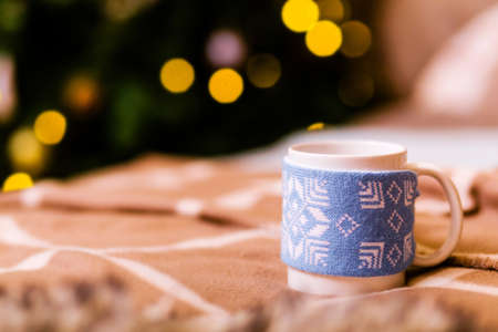 Evening atmosphere. A cup with a hot drink stands on a brown plaid against a background of yellow bokeh. Photoの写真素材