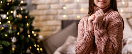 A young woman in a pink knitted sweater enjoys home comfort and New Year's atmosphere. Woman sitting...