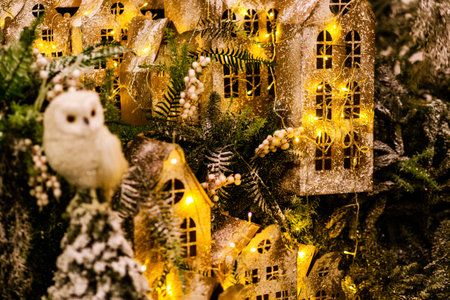 The toy owl sits on the background of toy wooden houses decorated with glowing garlands. New Year...
