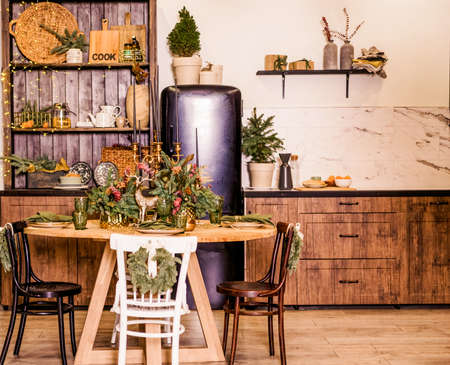 Festive kitchen in Christmas decorations. Candles, spruce branches, wooden stands, table laying. Photoの写真素材