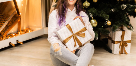 Girl in a white sweater and jeans posing with a New Year's gift in her hands