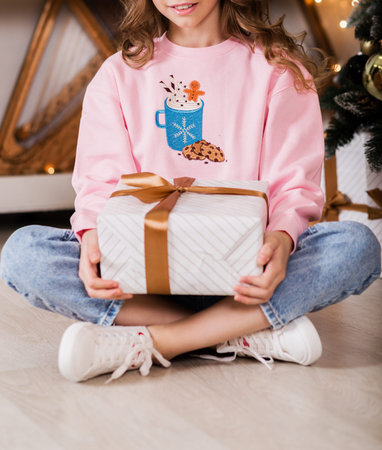 Girl in a pink sweater and jeans posing with a New Year's gift in her hands