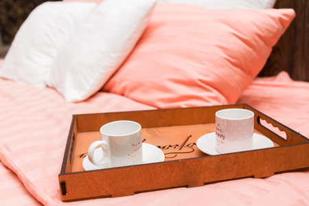 wooden tray with cups and saucers stands on the bed on a pink blanket