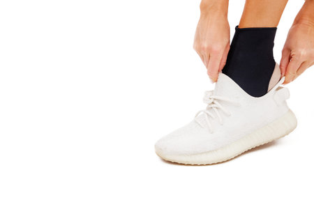 Girl puts sneakers on her leg with ankle brace on a white background