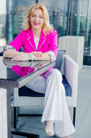 Successful woman entrepreneur in a magenta jacket posing on the terrace of a cafe in a business center. Business woman representation conceptの写真素材