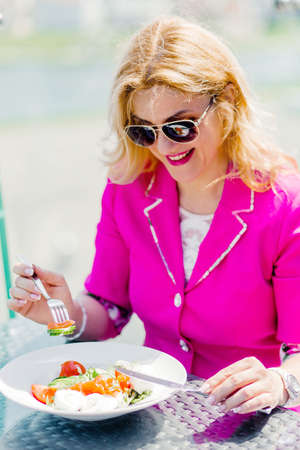 Beautiful woman eating fresh vegetable salad on the summer veranda of the restaurantの写真素材
