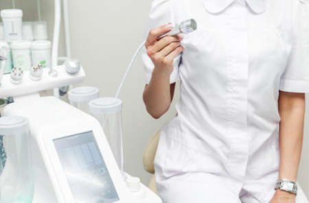 Cosmetologist posing next to a cosmetology machine and an ultrasonic head in his hand. Horizontal photoの写真素材