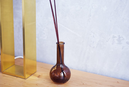 A rectangular lamp and a vase with aroma sticks stand against the background of a concrete wall....