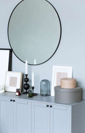 There is a chest of drawers near the gray wall with many interior details. There is a mirror on the wall, candles, boxes and a photo frame on the dresserの写真素材