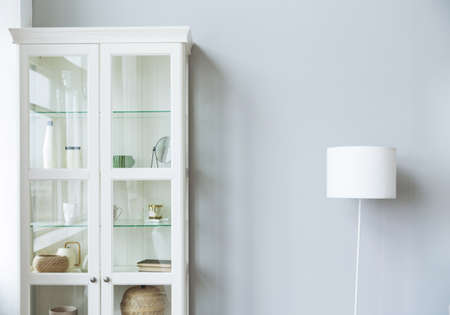 White cabinet with dishes, decor items and a lamp stand near a gray wallの写真素材