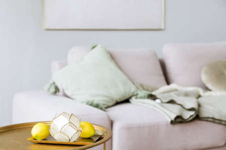 There is a sofa with pillows in front of the gray wall, next to the sofa there is a decorative table in gold color. There is a tray with lemons and a candlestick on the tableの写真素材